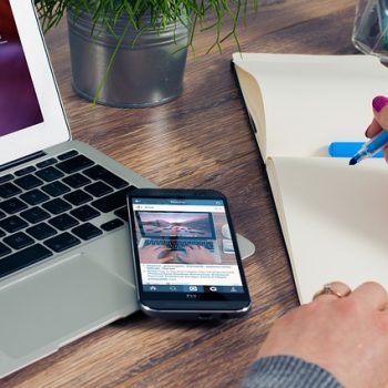 a laptop, a smartphone and hands writing on a notepad